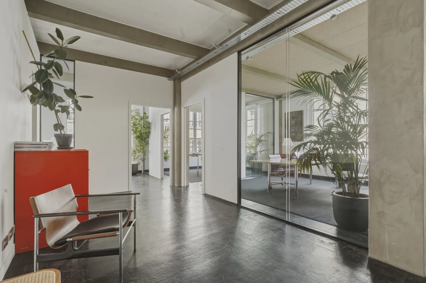Bureaux vitrés avec plantes, plafond en béton, fauteuil et meuble rouge